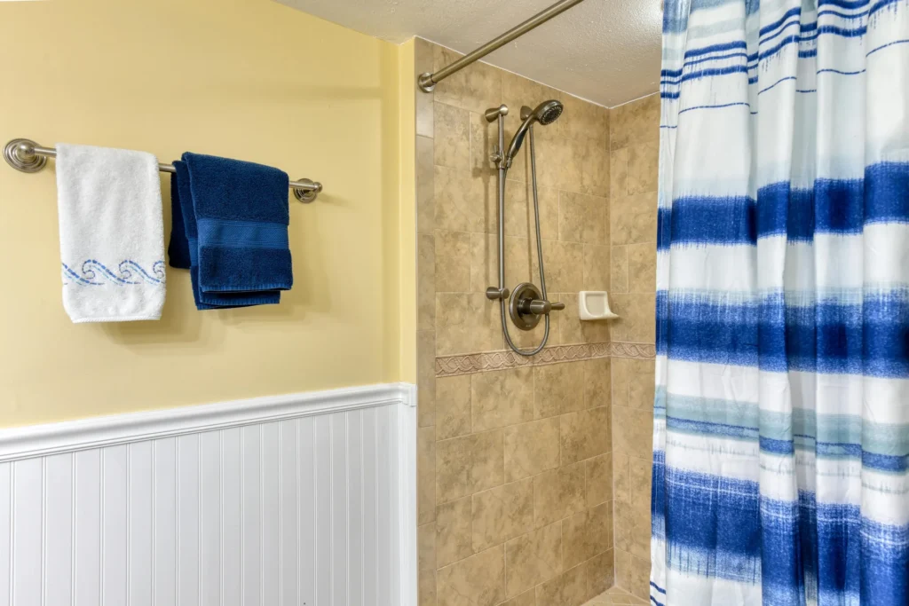 Walk-in shower features beige tile walls with decorative trim, brushed nickel fixtures, and a blue-striped shower curtain.