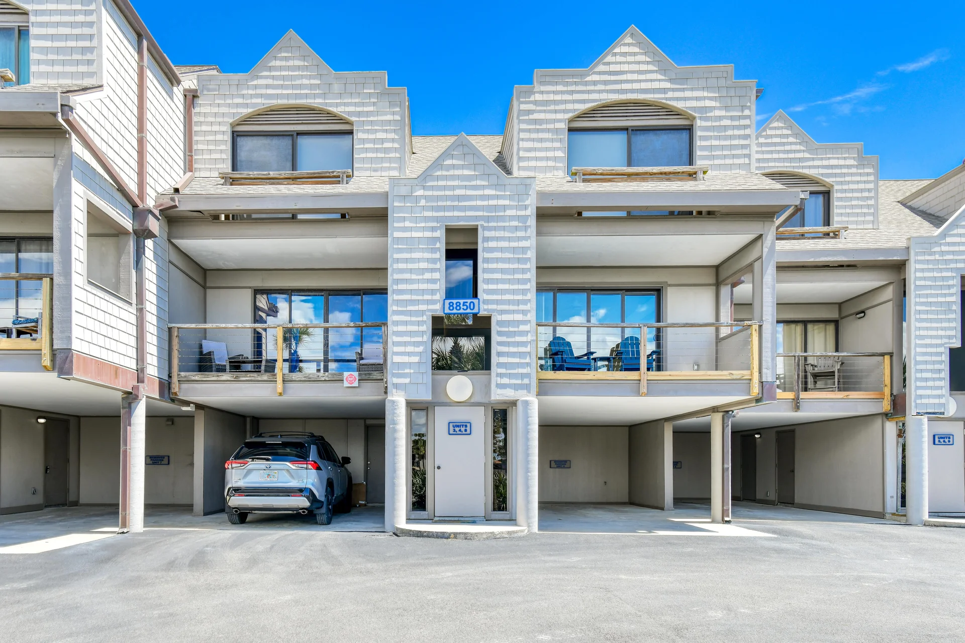 Covered parking spaces beneath the condo with concrete pillars and a central doorway framed by white shingle siding.