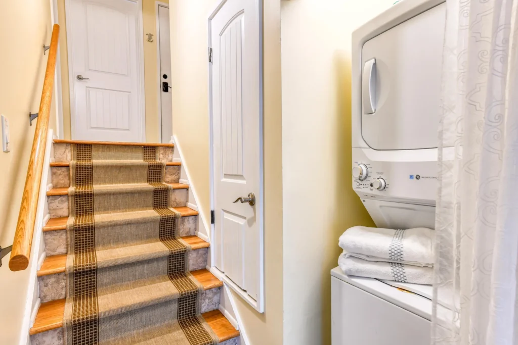 Carpet runner with brown and beige stripes covers wooden stairs flanked by a natural wood handrail and white doors.