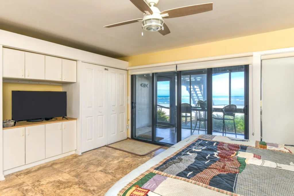 Bedroom features tiled floors, ceiling fan, built-in white cabinetry, and sliding glass doors opening to ocean views.