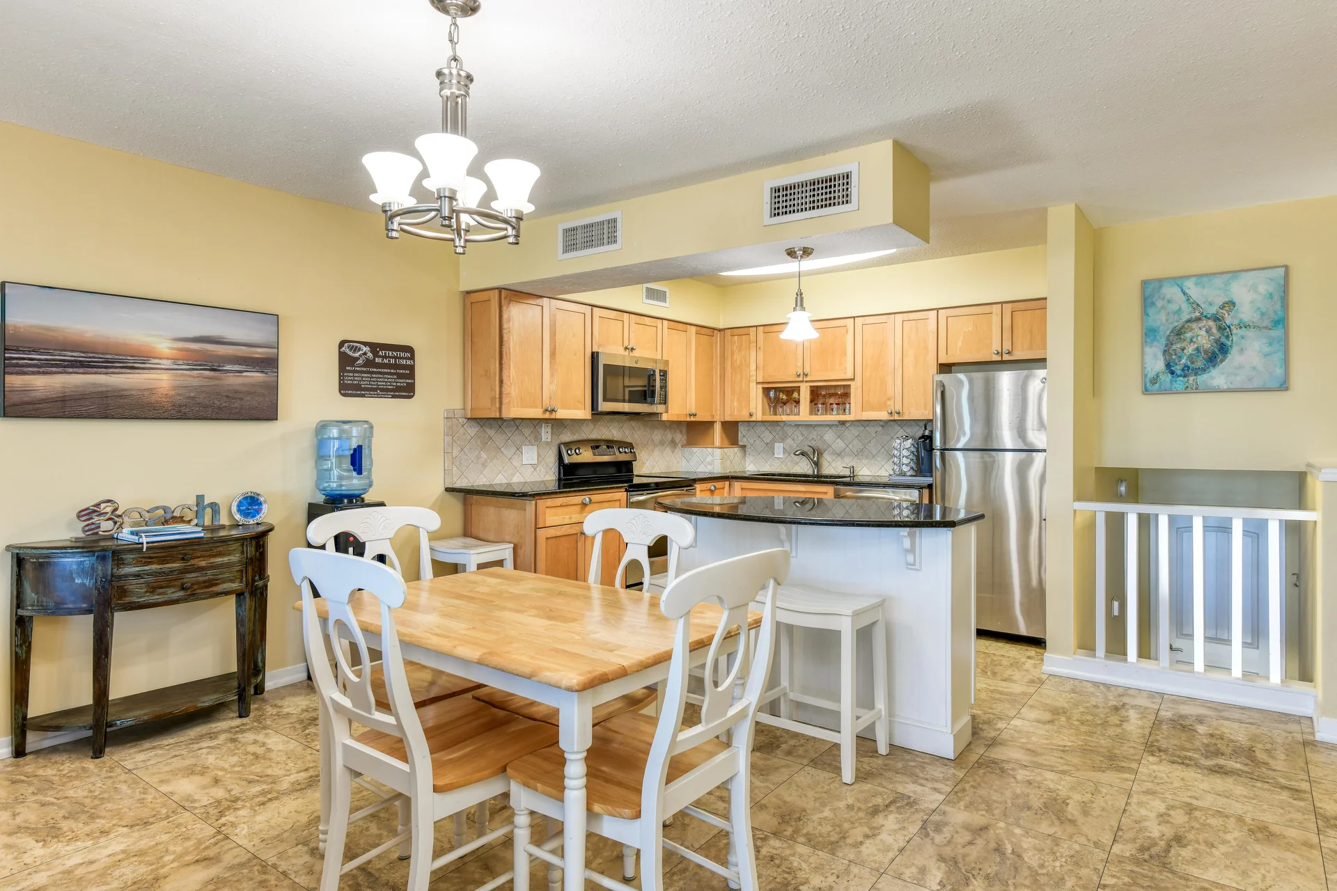 Dining area with wooden table and white chairs beside an open kitchen featuring light wood cabinets and granite counters.