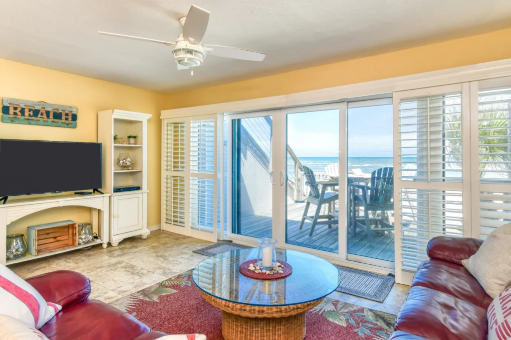 Living room with tiled floors, red leather sofas, wicker coffee table, and sliding glass doors to oceanfront balcony.