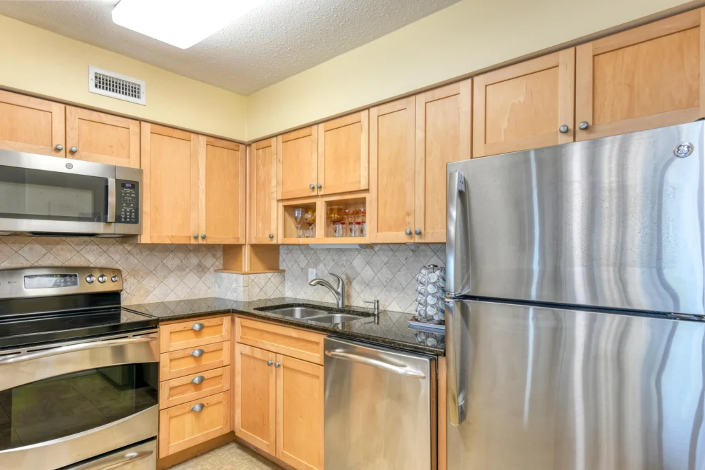 Light wood cabinetry frames stainless steel appliances, including a microwave, stove, dishwasher, and refrigerator.
