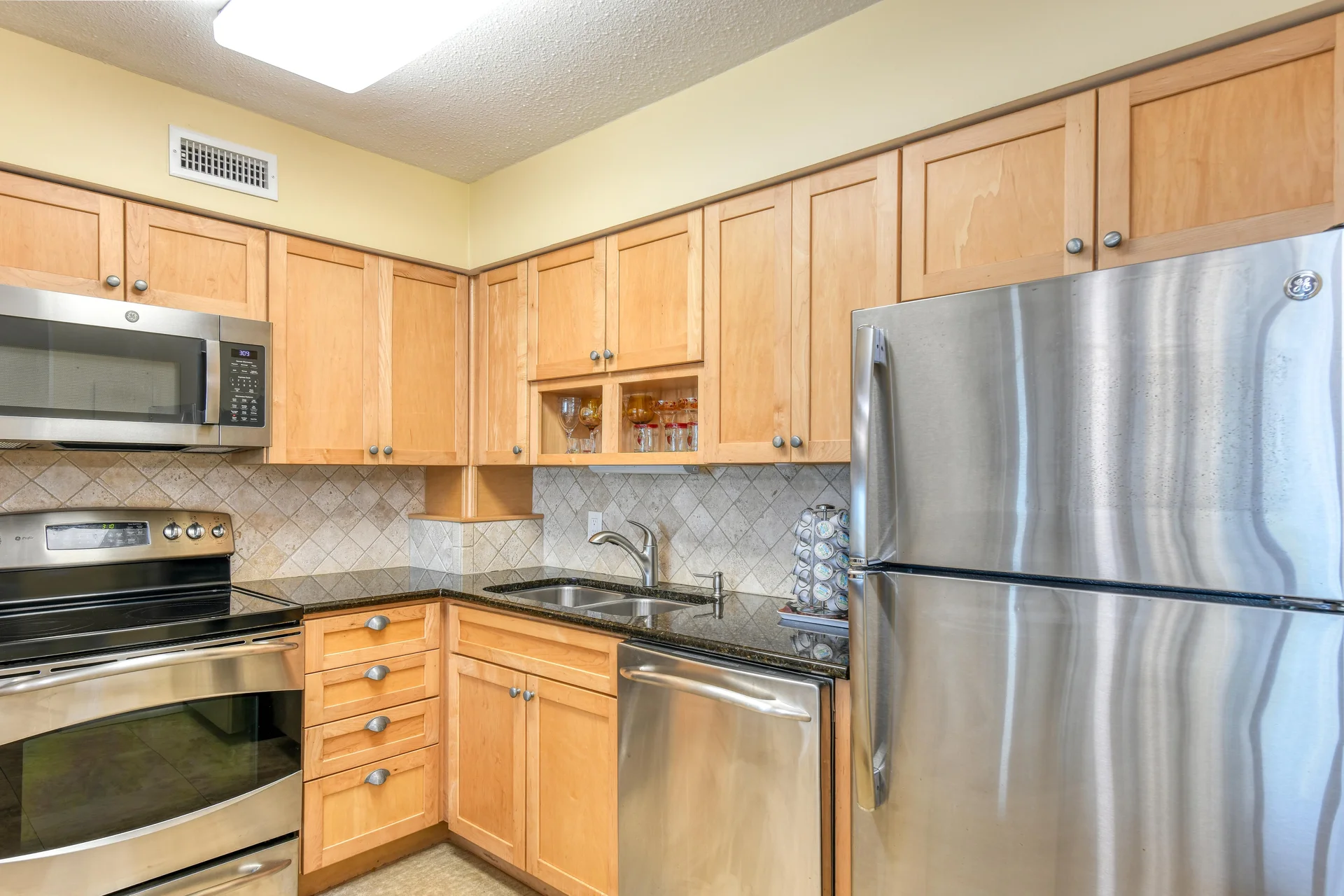 Light wood cabinetry frames stainless steel appliances, including a microwave, stove, dishwasher, and refrigerator.