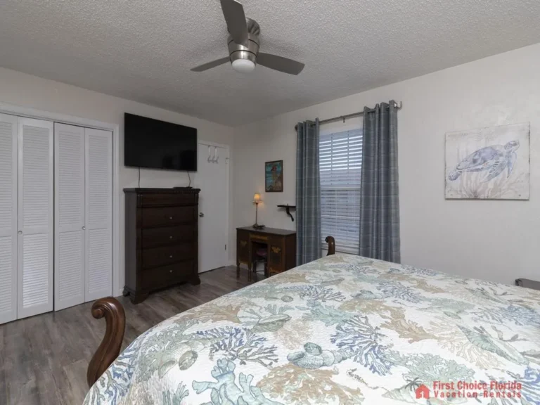 A wooden writing desk with a small lamp sits beneath a window framed by gray curtains in the bedroom.