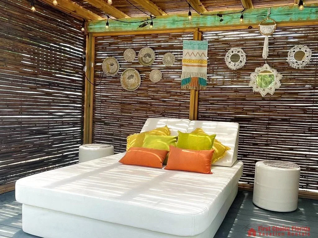 Daybed with white cushions and colorful pillows beneath a bamboo pergola adorned with woven wall hangings.