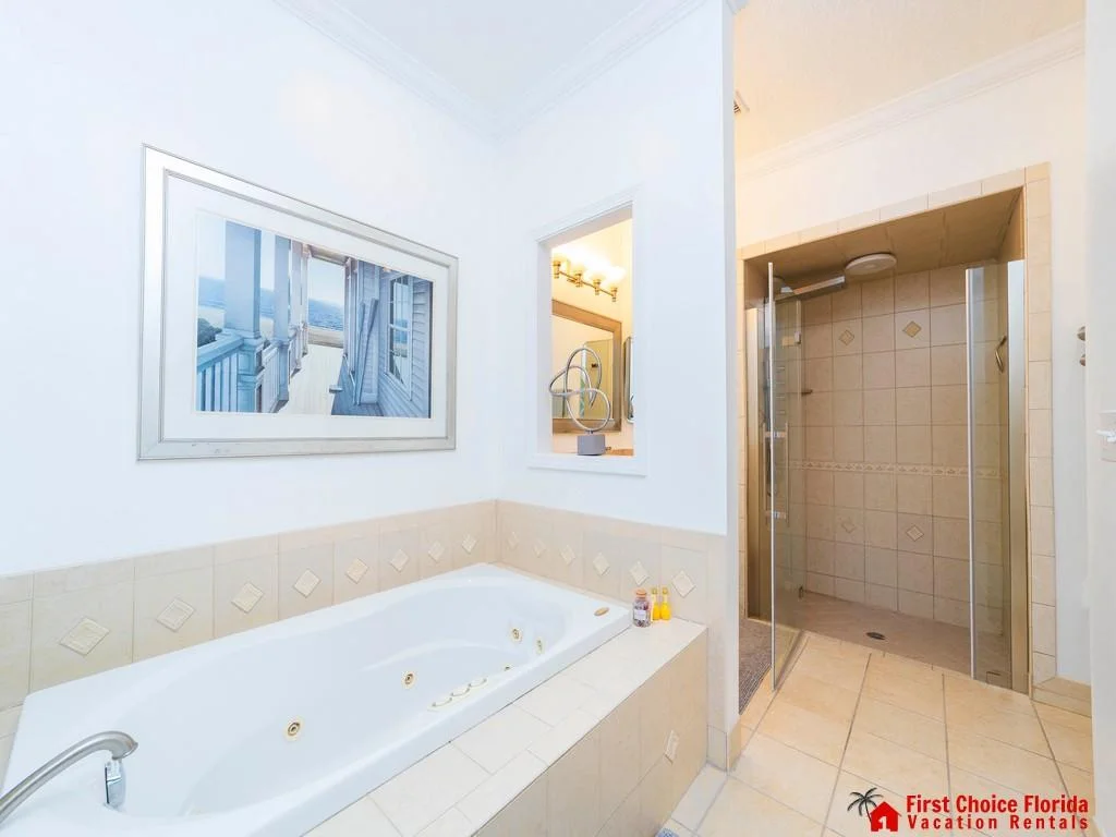 Bathroom features a tiled soaking tub with jets, walk-in glass shower, and ocean-themed artwork on white walls.
