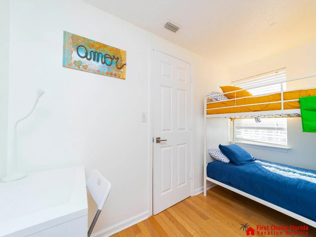 Bunk bedroom with white metal frame, mustard and navy bedding, hardwood floors, and a desk by the wall.