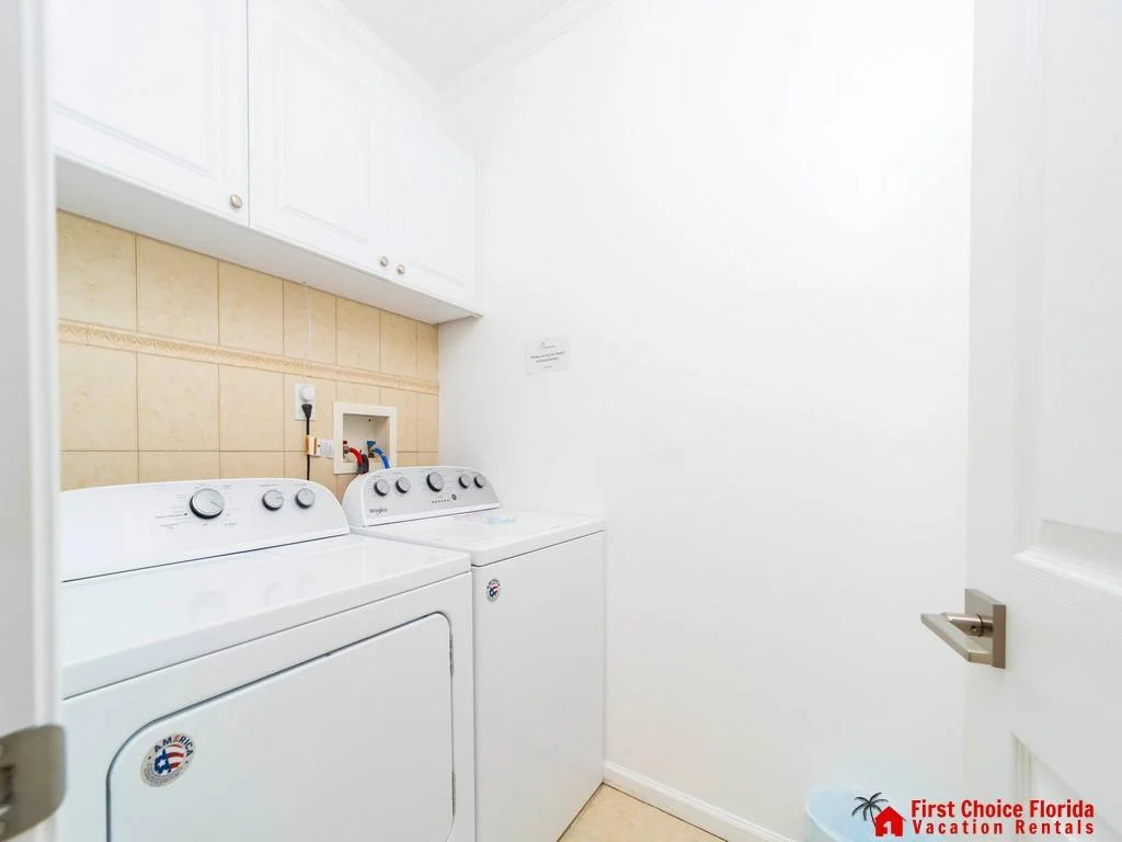Laundry area with white washer and dryer, beige tiled backsplash, and white cabinetry above.