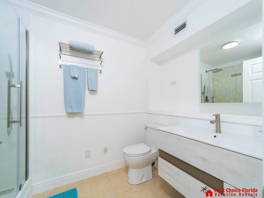 White bathroom with large mirror, modern faucet, glass-enclosed shower, and blue towels on metal rack.