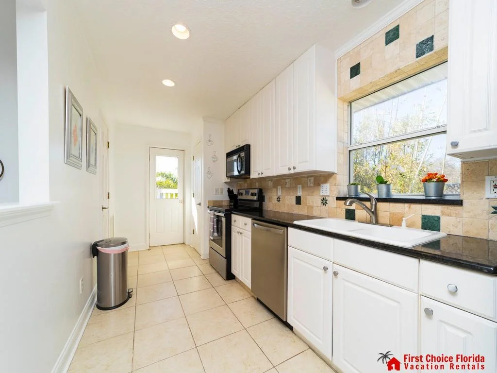 Galley kitchen featuring black granite counters, white cabinetry, stainless steel appliances, and tiled backsplash with green accents.