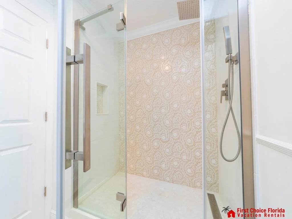 Walk-in shower with glass door, stainless steel fixtures, and beige patterned tile accent wall.