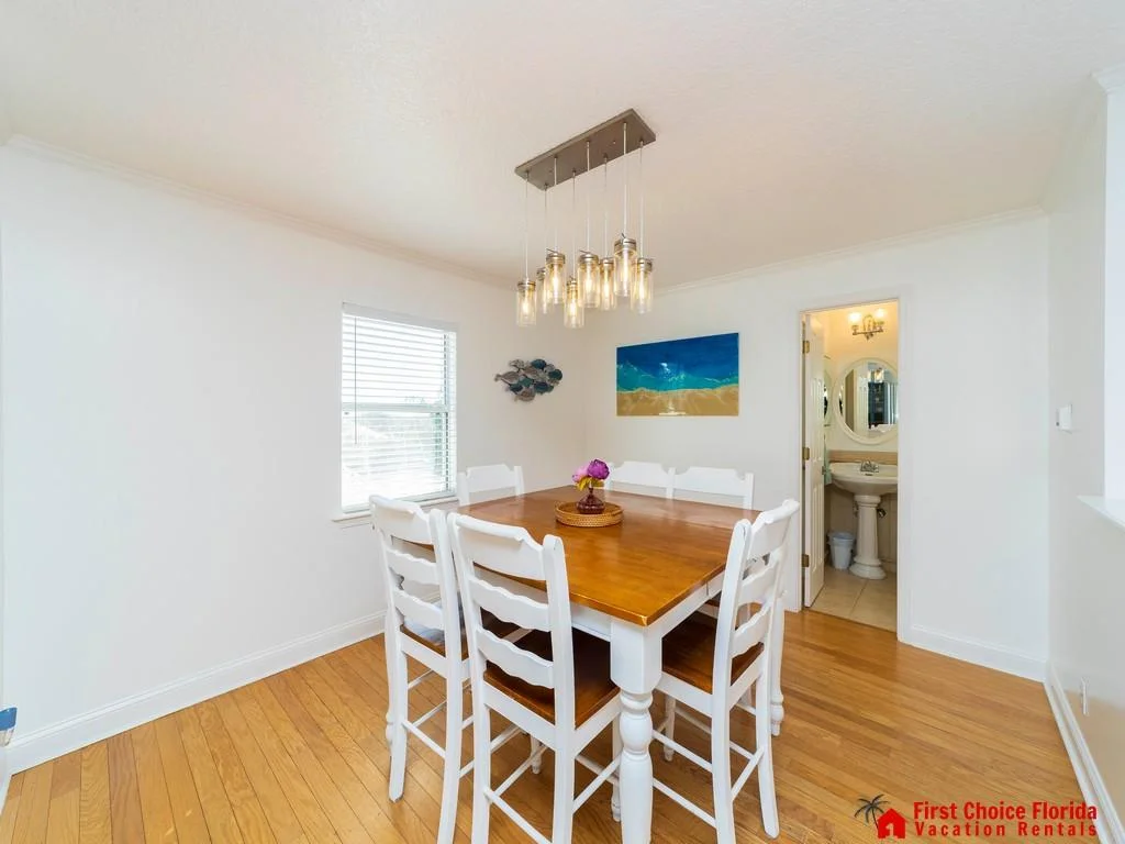 Dining area with honey-toned hardwood floors, white ladder-back chairs, wood table, modern pendant light, and adjacent half bath.