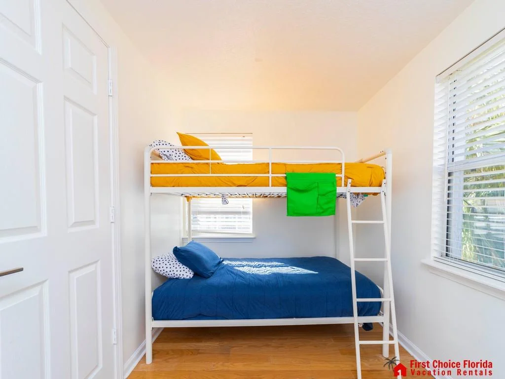 Bunk bed with white metal frame, mustard-yellow and navy bedding, polka-dot pillows, and natural wood floors.