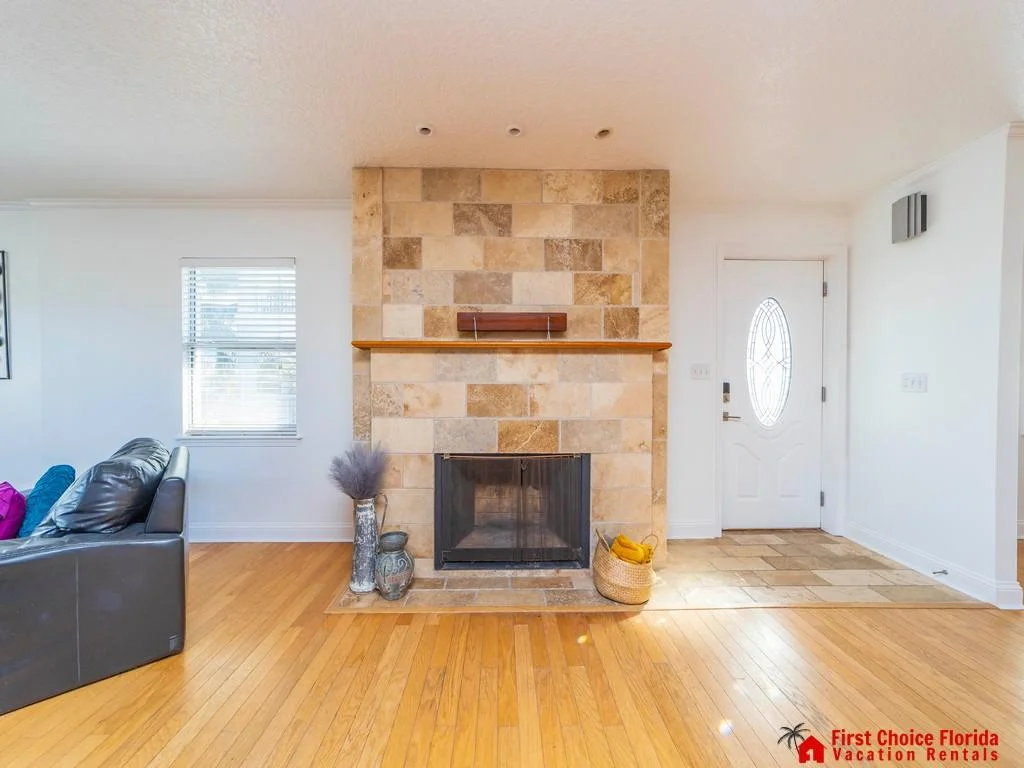 Sunlight highlights the hardwood floor, stone fireplace wall, and an entryway with tile flooring and oval glass door.