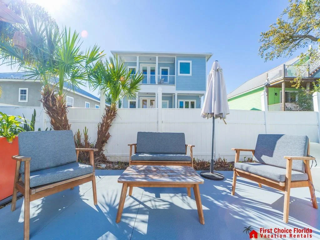Outdoor patio with gray cushioned wood chairs, matching coffee table, potted plants, and white privacy fence.