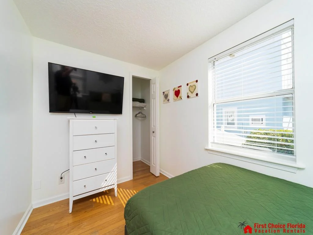 Natural light filters through white blinds onto the green quilted bedspread and hardwood floor in this bedroom.