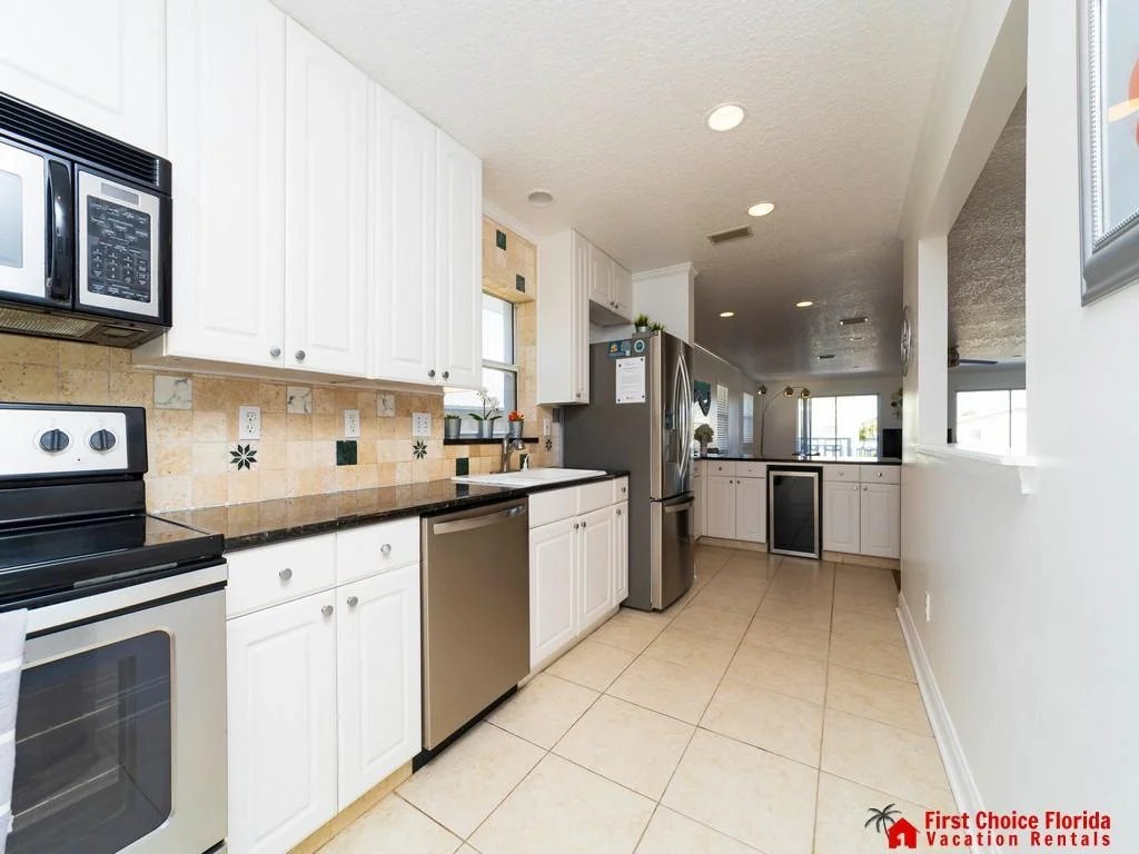 Galley kitchen with black granite counters, stainless steel appliances, beige tile backsplash, and ceramic floor.