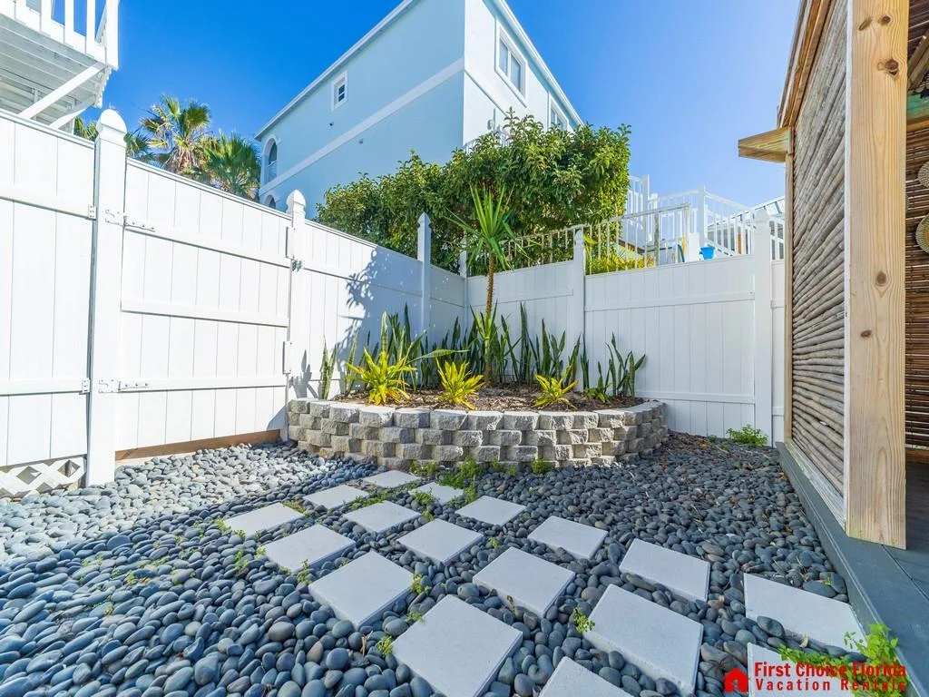 Private outdoor corner with white vinyl fencing, square stepping stones on black river rocks, and a raised plant bed.