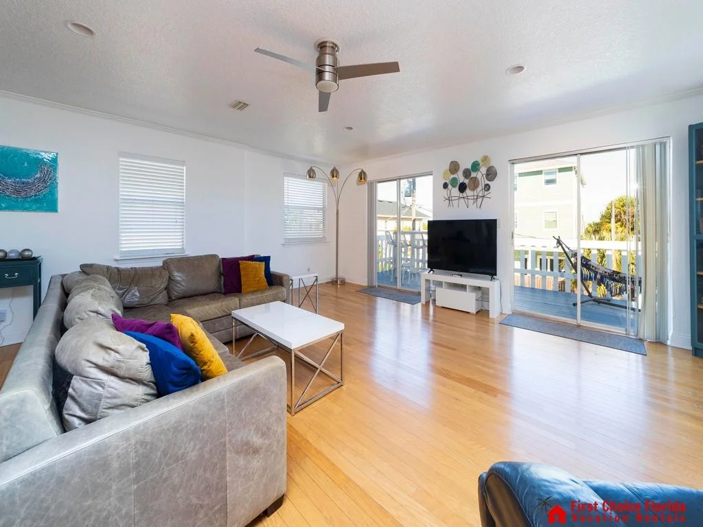 Living room with gray sectional, hardwood floors, metal-framed white coffee table, and sliding doors to balcony with hammock.