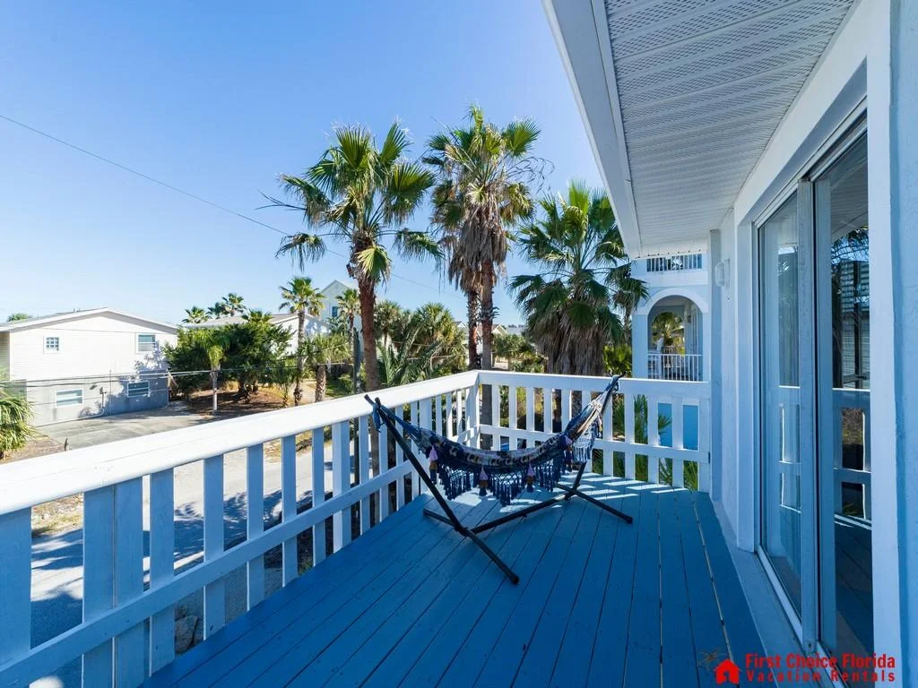 Second-floor balcony with blue painted wood floor, white railing, and a freestanding hammock under clear skies.