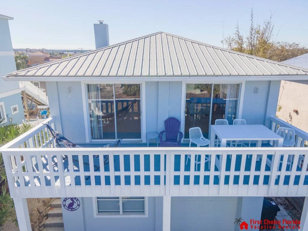 Upper-level balcony with white railing, purple Adirondack chair, white dining set, and two sliding glass doors.