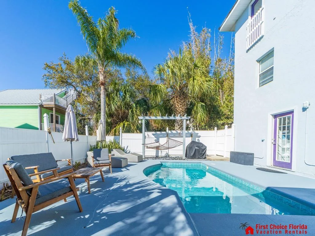 Blue-tiled pool with curved edges, surrounded by a light gray concrete deck and mid-century modern wood seating.