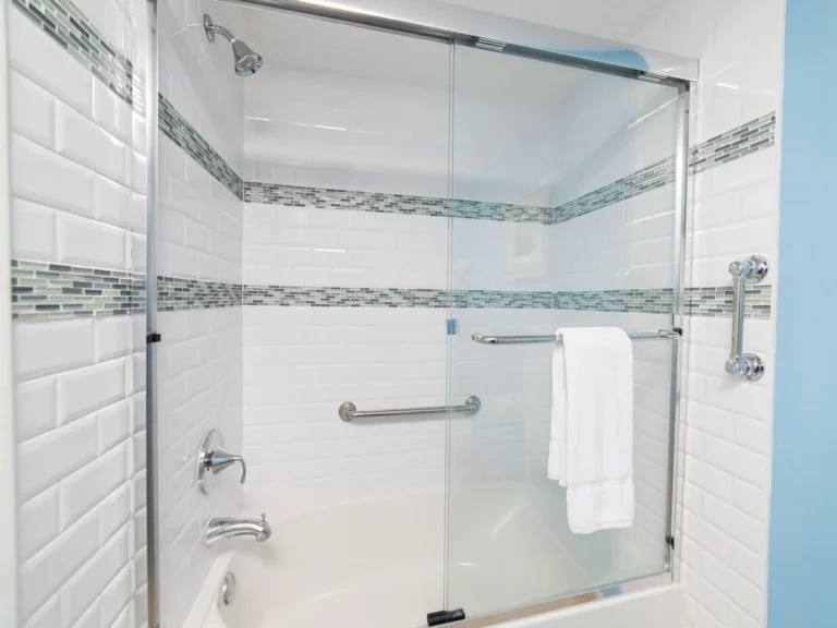 Bathroom shower with sliding glass doors, white subway tile, blue mosaic accent stripes, and chrome fixtures.