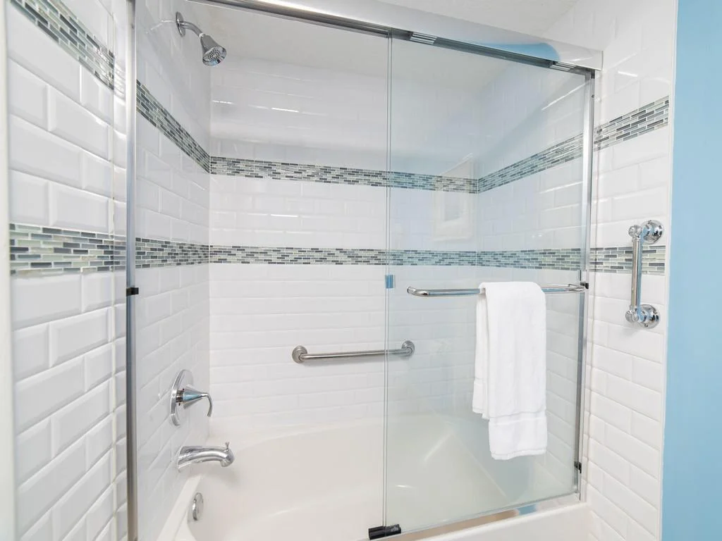 Bathroom shower with sliding glass doors, white subway tile, blue mosaic accent stripes, and chrome fixtures.