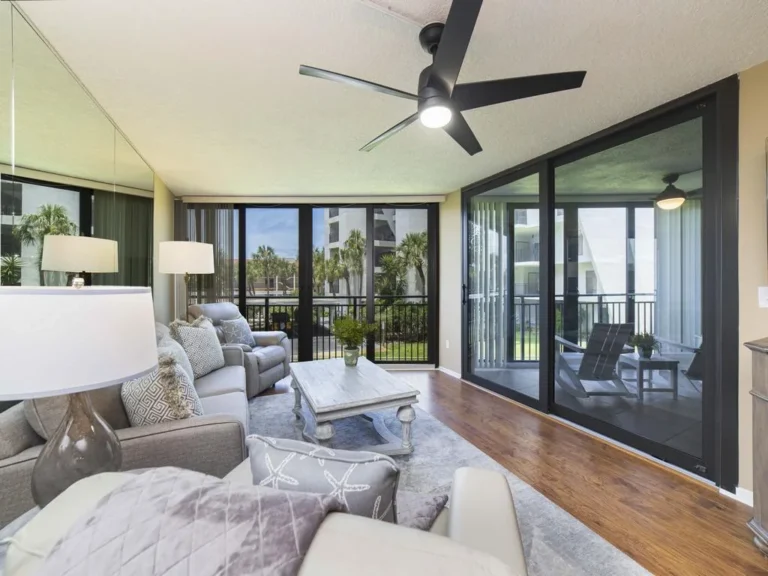 Sunlight filters through black-framed sliding glass doors onto hardwood floors in the living room with gray sofas and patterned pillows.