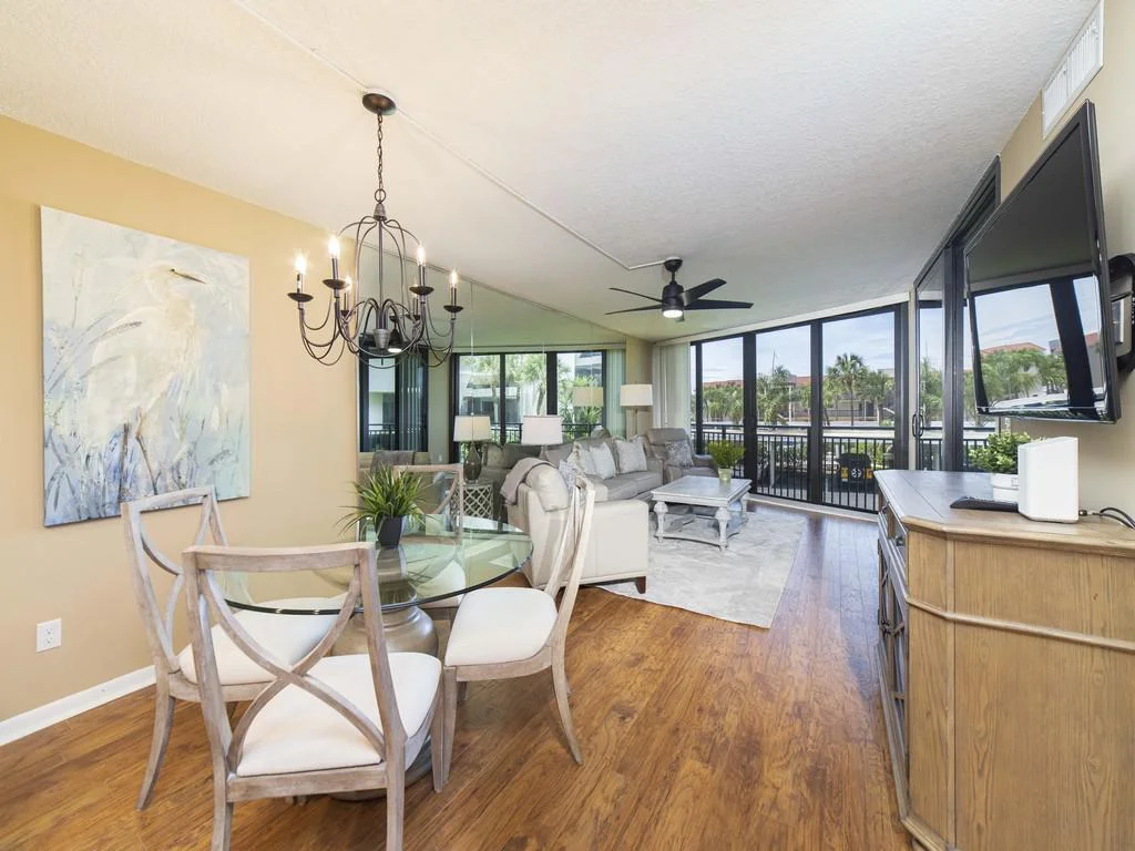 Glass sliding doors open to a balcony with black railing overlooking lush greenery beyond the living and dining space.