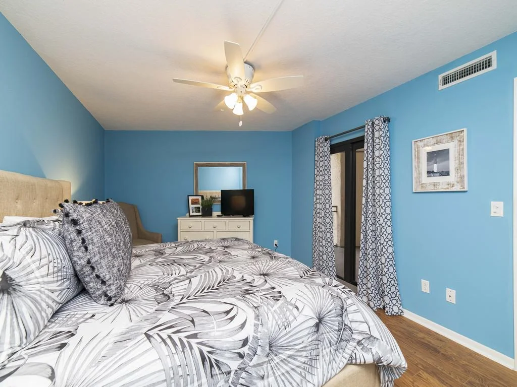 Bedroom with blue walls, patterned gray curtains, a ceiling fan, and a king bed with monochrome botanical bedding.