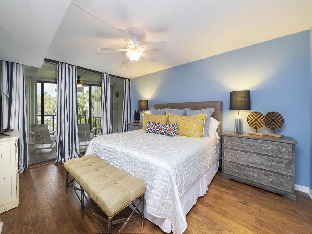 Master bedroom features a king bed with yellow and patterned pillows, blue walls, and sliding doors to a balcony.