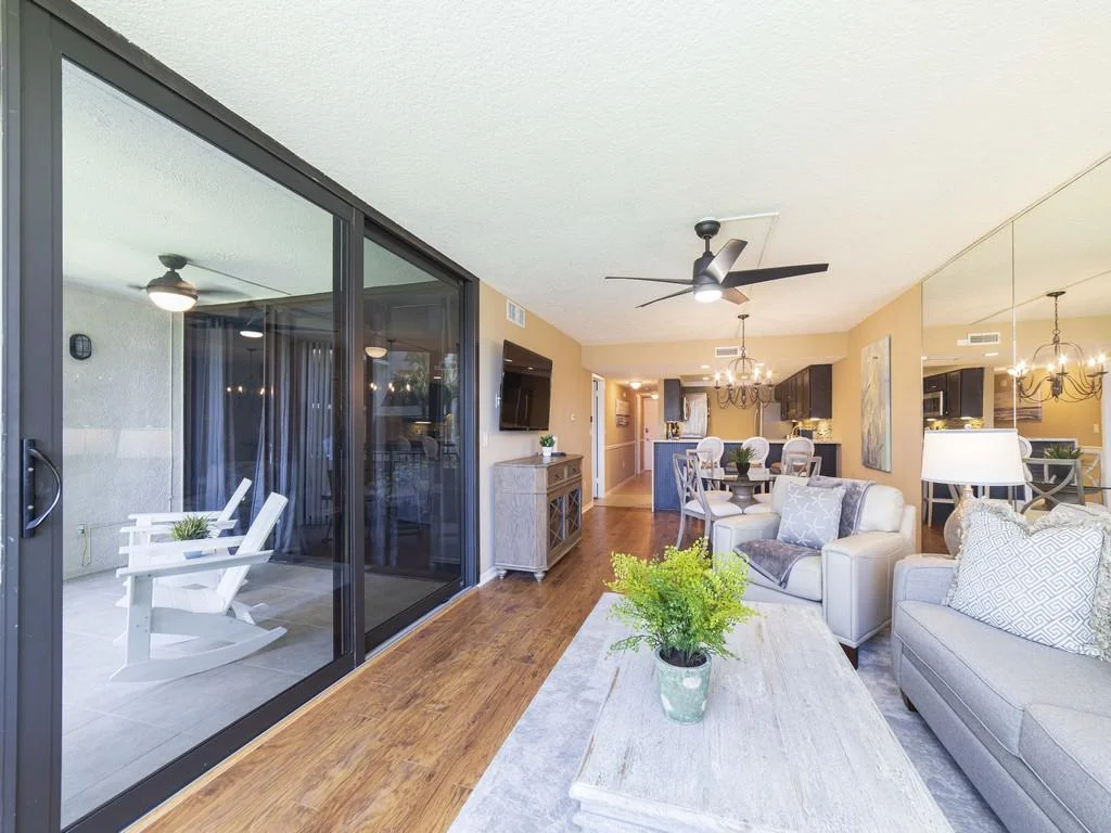 Sliding glass doors open from the living room to a covered balcony with white rocking chairs and a ceiling fan.