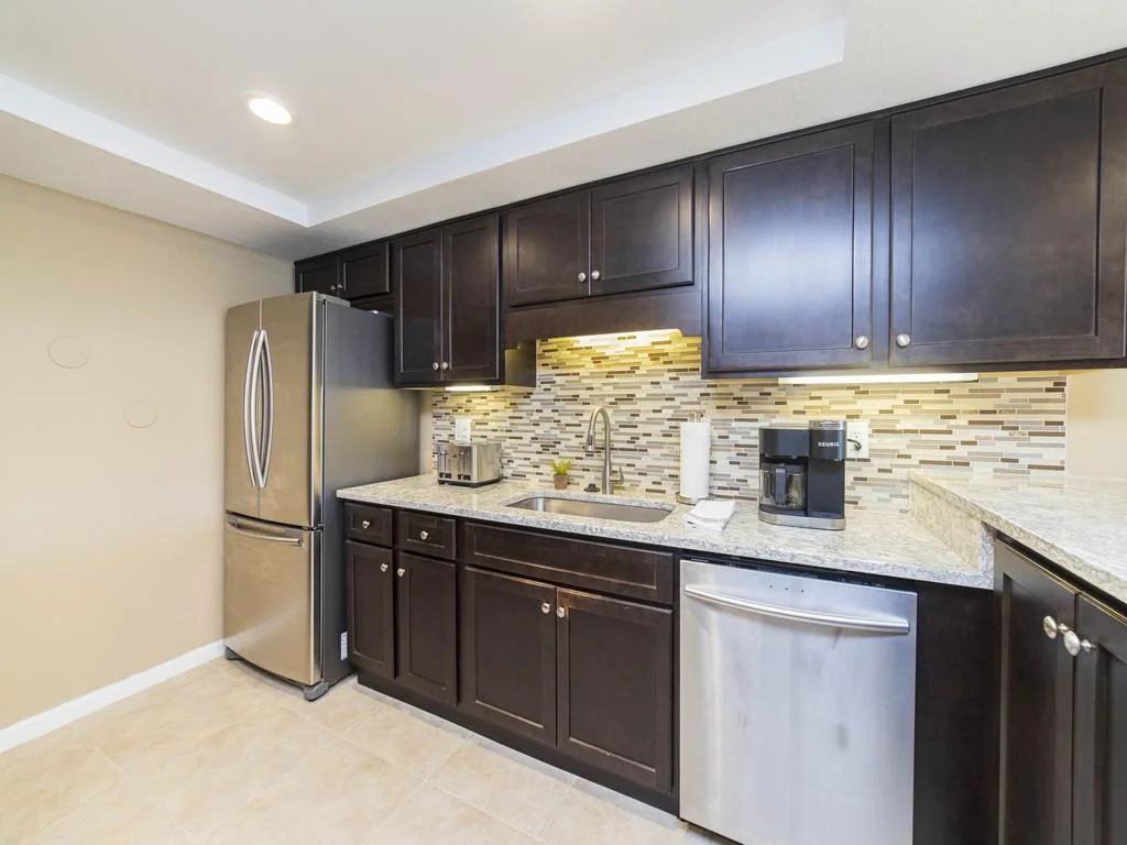 Dark wood cabinetry contrasts with the mosaic tile backsplash and stainless steel appliances in the kitchen.