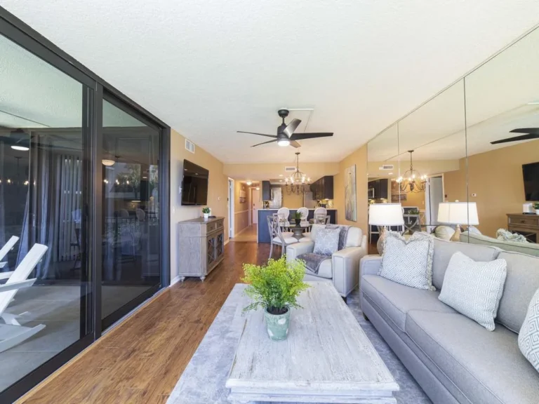 Open living and dining area with hardwood floors, gray upholstered seating, and large mirrored wall reflecting light.