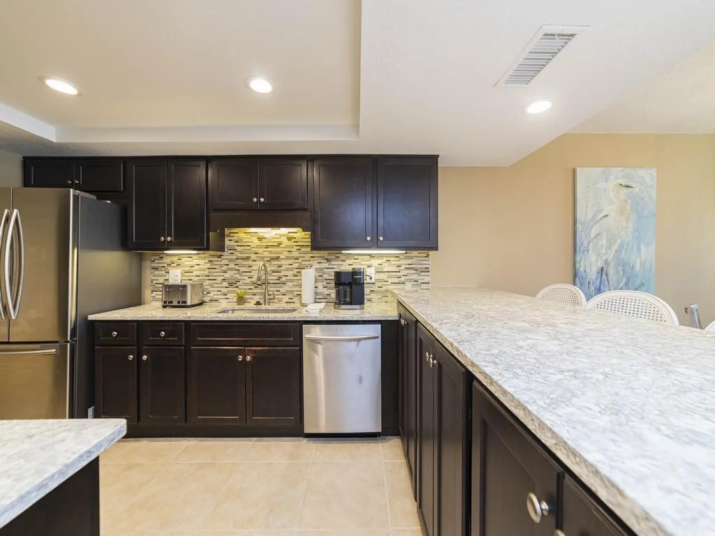 Granite countertops extend into a breakfast bar with cane-back chairs under warm recessed lighting.