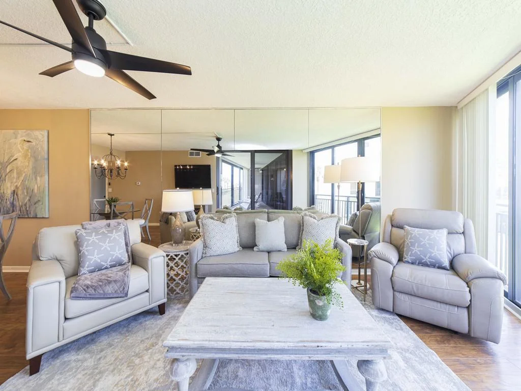 Living room with light gray sofa, leather armchairs, mirrored wall, and sliding glass doors to balcony.