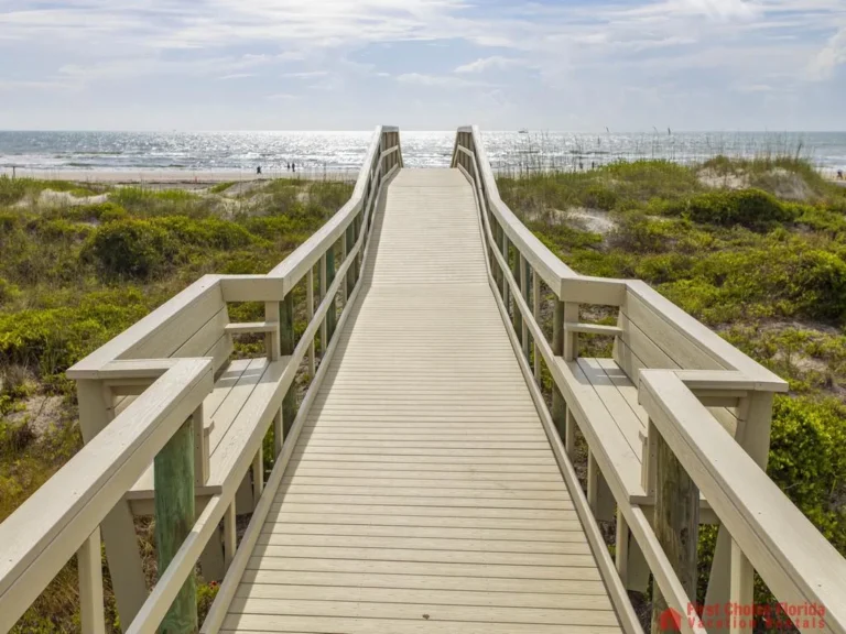 Boardwalk with built-in benches leads over coastal dunes to the sandy beach and shimmering ocean beyond.