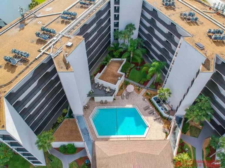 Aerial view of the gated community’s central pool area with lounge chairs, umbrellas, and surrounding palm trees.