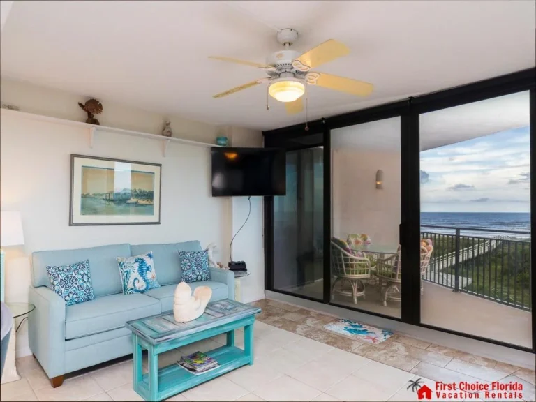 Flat-screen TV mounted above a corner shelf, with tiled floor and sliding glass doors to the balcony.