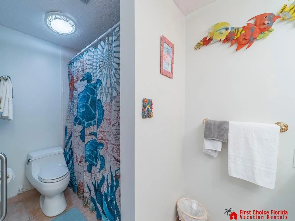 Bathroom with tiled floor, turtle-patterned shower curtain, towel rack, and colorful fish wall decor.