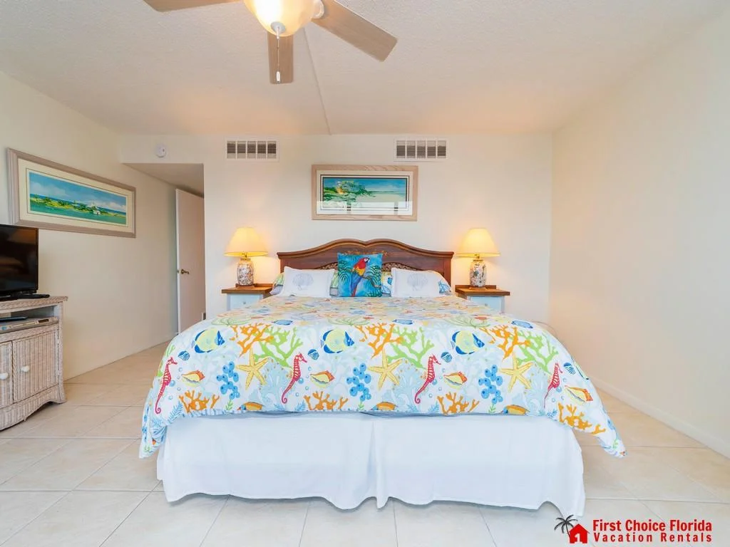 King bed with seashell and coral-patterned bedding, wooden headboard, tiled floor, and bedside lamps.