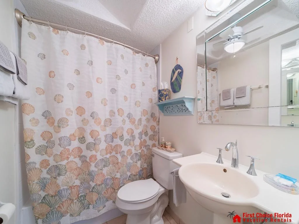 Bathroom features a curved shower rod with a seashell-patterned curtain and a white sink with silver fixtures.