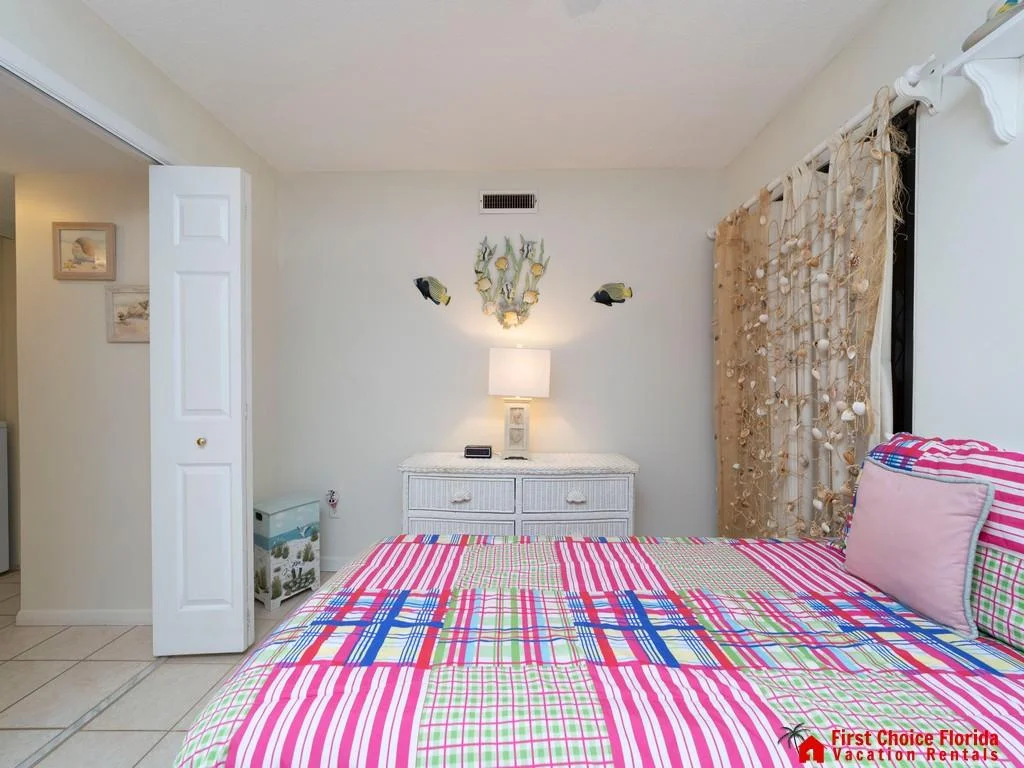 Bed with striped and checkered bedding sits beside a white wicker dresser and seashell curtain on tiled floor.