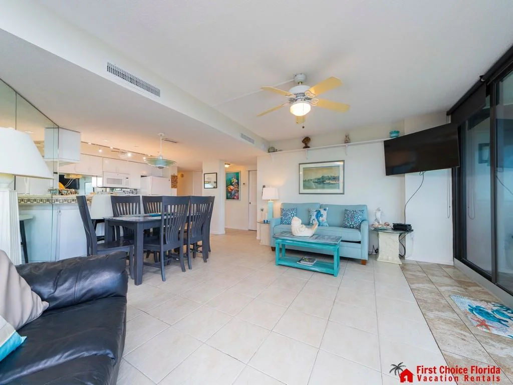 Sliding glass doors open to an oceanfront tiled living room with a mounted TV and coastal decor accents.