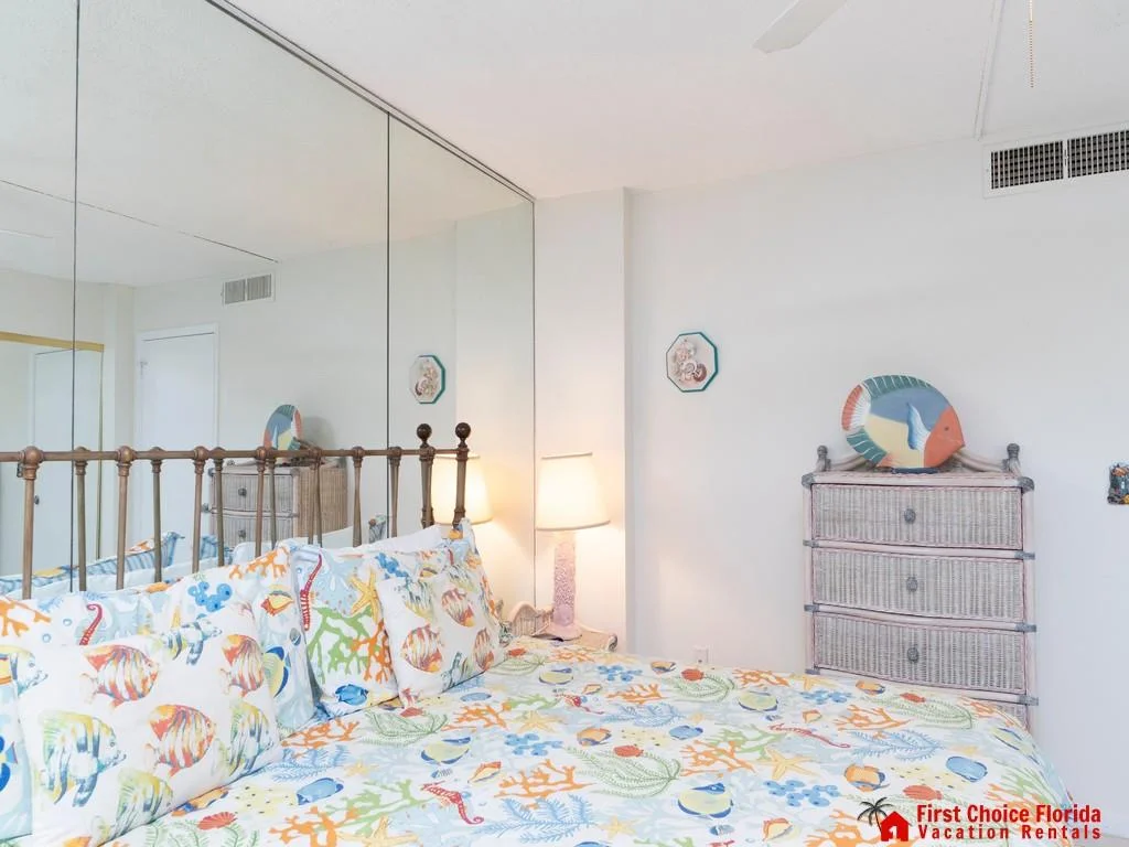 Metal bed frame with coral and sea life patterned bedding sits beside a lamp and wicker dresser with fish decor.