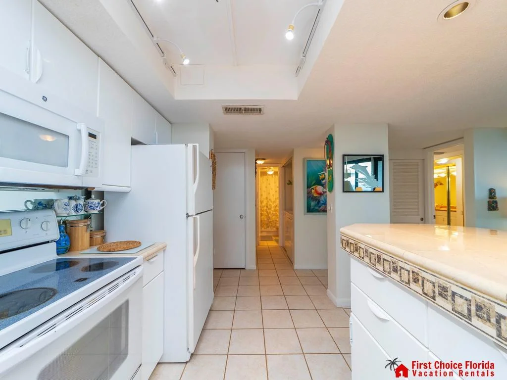 White cabinetry and appliances line the tiled kitchen with a beige countertop featuring decorative tile trim.