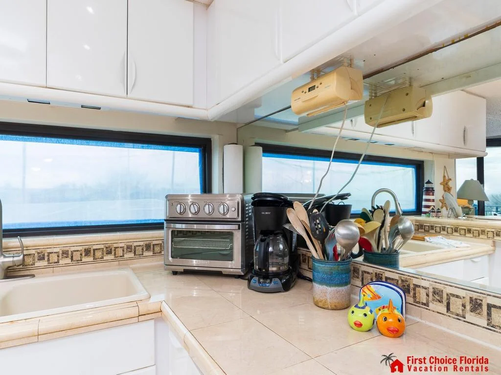 Cream-colored tile countertops with decorative trim surround a corner sink beneath a wide horizontal window.