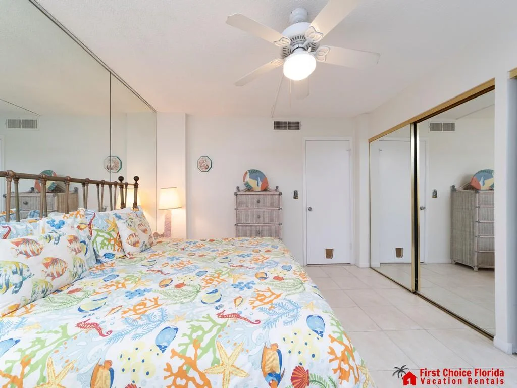 Bedroom with tile flooring, mirrored closet doors, a ceiling fan, and a bed dressed in colorful sea life bedding.